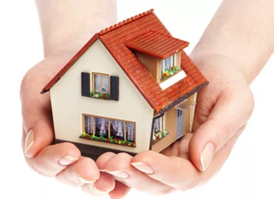 A person holding a small house with cream walls